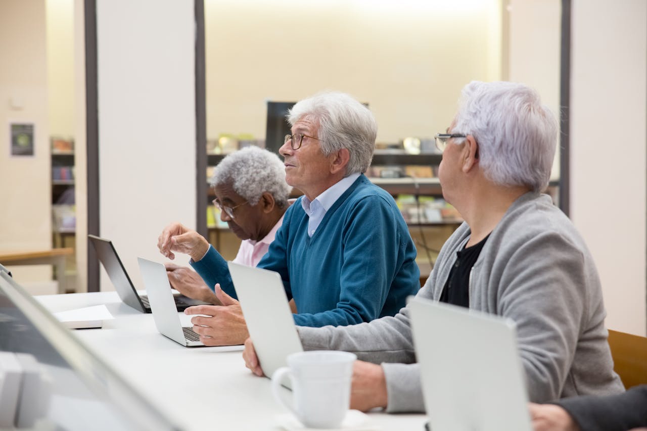 Elderly men using laptops in a modern tech class, learning digital skills.