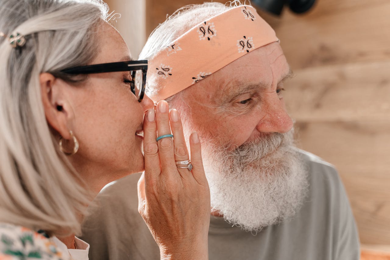 Close-up of an elderly couple sharing a secret in a warm indoor setting.