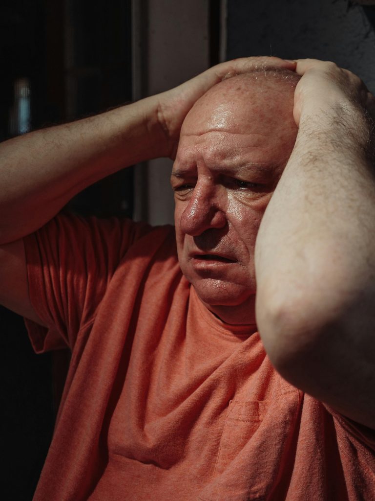 Portrait of an elderly man showing intense emotional distress with hands on head.